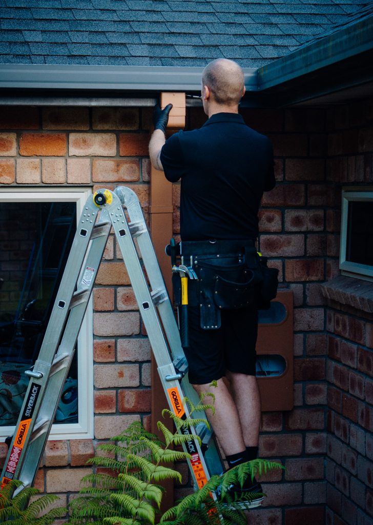 Connect Property Services technician repairing or inspecting a gutter downpipe on a brick home in Auckland